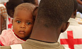 Foto: Haitianisches Baby schaut einem Rotkreuzhelfer über die Schulter.